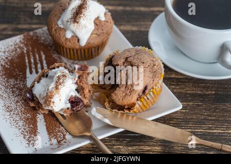 Süßer Kirschmuffin mit Eis und weißer Tasse mit Tee auf einem Holzhintergrund, Nahaufnahme Stockfoto