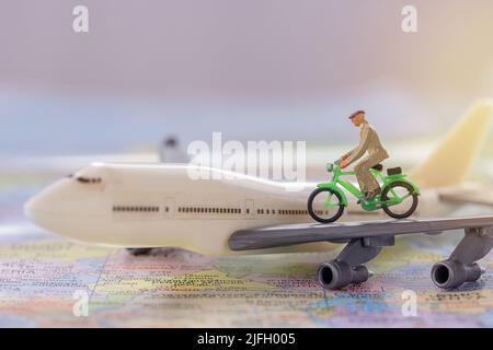 Miniatur Menschen - Figur businessmans Radfahren auf weißem Flugzeugmodell mit verschwommenem Weltkarte Hintergrund. Business Finance und Reisekonzept. Stockfoto