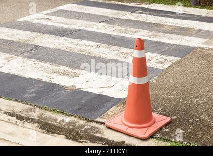 Nahaufnahme leuchtend orange Verkehrskegel stehen in einer Reihe auf Asphalt. Beton Bürgersteig mit gelb rot und weiß Verkehrsschild. Stockfoto