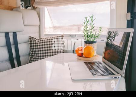 Innenansicht des modernen Wohnmobil-Fahrzeug mit leptu eleganten weißen Tisch und Laptop darauf. Konzept von Urlaub und Heimat, um das Leben in einem Kleinbus abseits des Stromnetzes zu leben. Wo Stockfoto