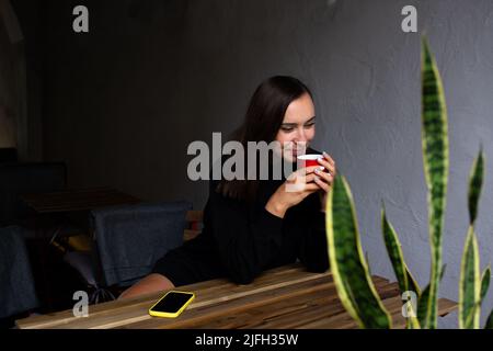 Allein junge Frau, die an einem regnerischen Tag in einem Terrassencafé einen Drink trinkt Stockfoto