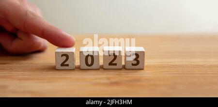 2023 Happy New Year Konzept. 2023 Zahl auf Holzwürfel mit Finger, um Ziffer 2 zu zeigen. Neues Paar, Ehe, Plan, Geschäft, Karriere, Ziel, Erfolg. G Stockfoto