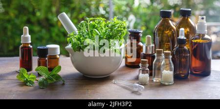 Kräutermedizin, alternative Heilung. Naturapotheke und Homöopathie Produkte. Frische Kräuter im Mörser und Glasflaschen auf Holztisch, Banner. Stockfoto