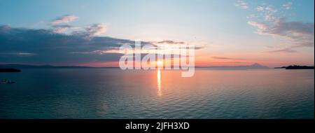Sonnenuntergang über dem ruhigen Ozean Panoramablick. Dramatische, magische Sonnenaufgangslandschaft in der Ägäis, Griechenland. Sonnenreflexion auf dem Wasser. Orange und blaue Farbe Sha Stockfoto