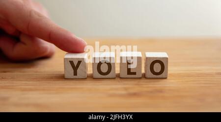 Yolo-Konzept. Wort yolo auf Holzwürfel mit Finger zeigt Buchstabe y. You Only Live Once Phrase, Botschaft, um den Tag zu ergreifen, positive Lebensweise, folgen Stockfoto