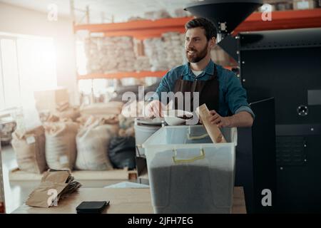 Uniformierte Arbeiter verpackt geröstete Kaffeebohnen in Verpackungen zum Verkauf und zum Suchen Stockfoto