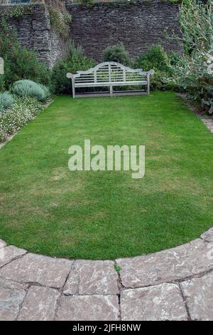 Verzierte Holzgartenbank vor der Steinmauer im Garten von Hestercombe. Stockfoto