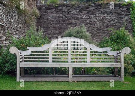 Verzierte Holzgartenbank vor der Steinmauer im Garten von Hestercombe. Stockfoto