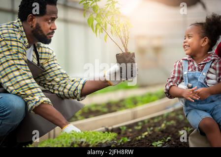 Porträt eines afrikanischen Mannes, der den Kindern beibringt, Setzlinge im Gewächshaus zu Pflanzen Stockfoto