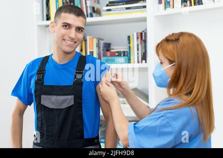 Lachender Mann nach der dritten Impfung gegen Covid 19 mit Krankenschwester Stockfoto