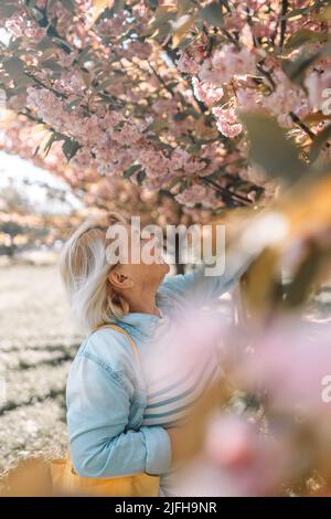 Schöne 50s Frau genießen sonnigen Tag im Park während der Kirschblütensaison an einem schönen Frühlingstag Stockfoto