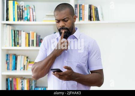 afroamerikanische reife Erwachsene Geschäftsmann denken über Nachricht am Telefon im Büro Stockfoto