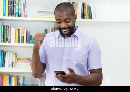 afroamerikanischer reifer erwachsener Geschäftsmann erhält am Telefon im Büro eine Nachricht mit guten Nachrichten Stockfoto