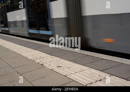 Teil einer Straßenbahn in Bewegung an einer Straßenbahnhaltestelle in einer Stadt Stockfoto