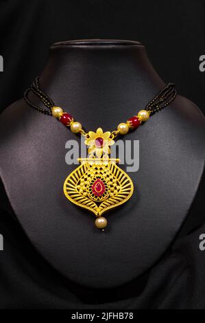 Closeup Temple Gold Halskette (Mangalsutra) mit schwarzen Perlen und roten Edelsteinen auf schwarzem Hintergrund Stockfoto