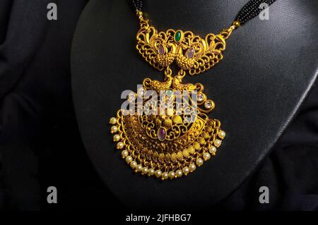 Closeup Temple Halskette Gold (Mangalsutra) mit schwarzen Perlen. Rote und grüne Edelsteine, Stein auf schwarzem Hintergrund Stockfoto