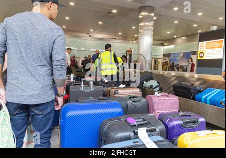 Verspätungen am Flughafen Heathrow; Gepäckabfertiger, die Stapel von Gepäck im Reisechaos verwalten, Gepäckabholung am Terminal 3, Flughafen London, Großbritannien Stockfoto