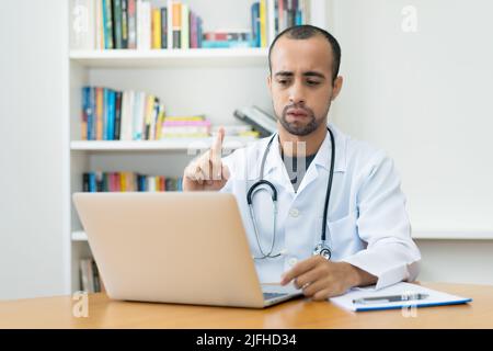 Ein lateinamerikanischer Arzt warnt den Patienten bei einem Videoanruf am Computer im Krankenhaus Stockfoto