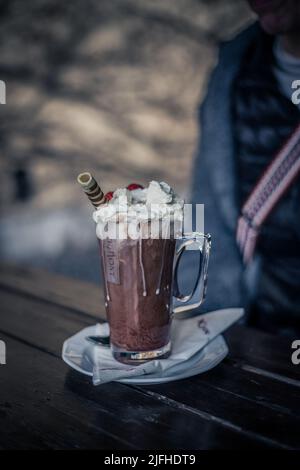 Ein Glas Kaffee mit Schlagsahne und Schokolade auf einem Holztisch Stockfoto