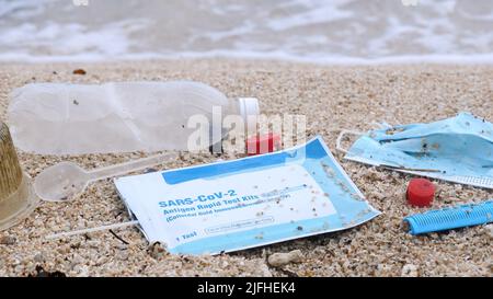 Abfall während COVID-19. Medizinische Gesichtsmasken und Covid-Test am Strand mit Wellen auf dem Hintergrund verwendet. Verschmutzung durch Ozeanplastik Stockfoto