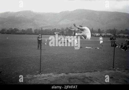 1952, historisch, draußen auf einem Grasfeld, mit Hochlandbergen in der Ferne, ein älterer männlicher Student in der Luft, der den Hochsprung macht, Schottland, Großbritannien. Stockfoto