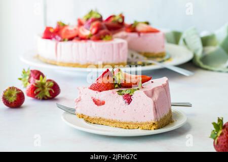 Eine Scheibe Erdbeerkäsekuchen mit dem Rest des Kuchens dahinter. Stockfoto