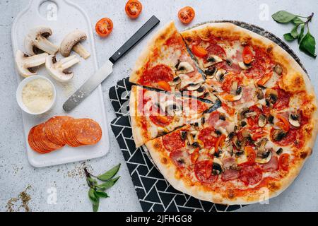 Salami und Pilzpizza auf einem Tisch neben rohen Zutaten. Draufsicht. Stockfoto