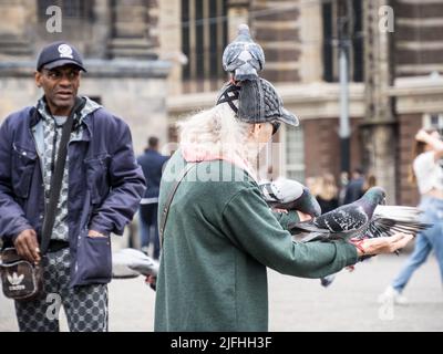 Touristen füttern Tauben am Dam-Platz, Amsterdam Stockfoto