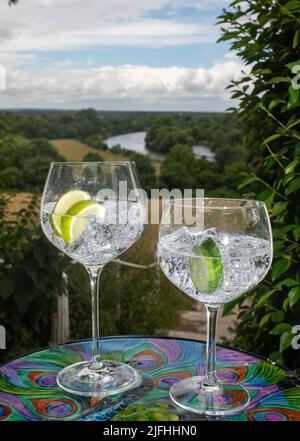 Zwei große und kleine Gin-Gläser mit Eiswürfeln und Limettenscheibe mit Blick auf die Brüstung von Richmond Hill und die Themse Stockfoto