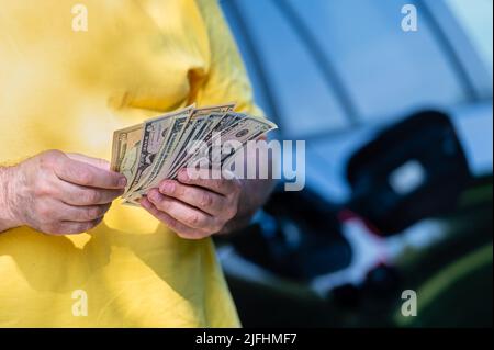 Mann mit Dollarscheinen auf dem Hintergrund eines Autos mit offenem Gastank, Nahaufnahme der Hände Stockfoto