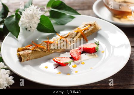 Gerollter Pfannkuchen mit Erdbeere auf weißem Teller Stockfoto