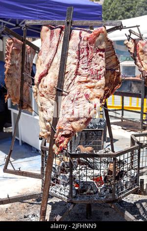 Argentinisches Fleisch, das in einer Metallstruktur mit einem Feuer unter dem Grill gegrillt und mit dem Rauch und der Hitze, die vom Feuer abgegeben wird, gebraten wird. Stockfoto