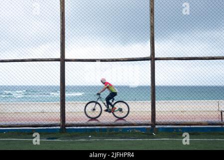 Silhouetten von Radfahrern, die bei Regen hinter dem Sportzaun vorbeifahren. Salvador, Bahia, Brasilien. Stockfoto