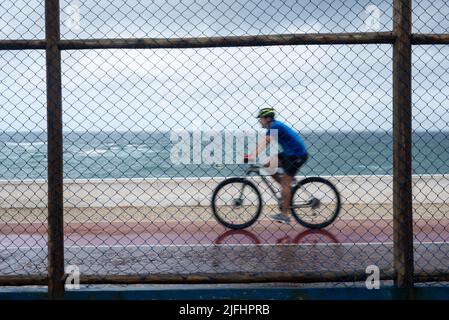 Silhouetten von Radfahrern, die bei Regen hinter dem Sportzaun vorbeifahren. Salvador, Bahia, Brasilien. Stockfoto