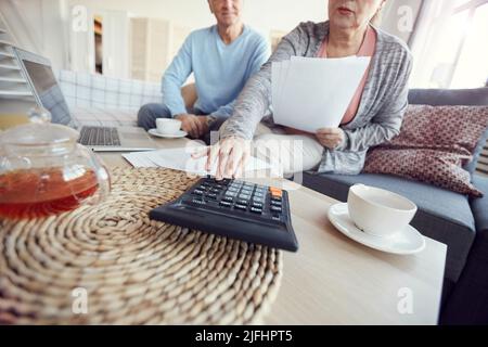 Nahaufnahme eines vielbeschäftigten verheirateten Seniorenpaares mit Taschenrechner bei der gemeinsamen Planung des Familienbudgets, Blickkontakt Stockfoto
