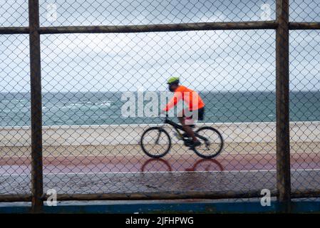 Silhouetten von Radfahrern, die bei Regen hinter dem Sportzaun vorbeifahren. Salvador, Bahia, Brasilien. Stockfoto