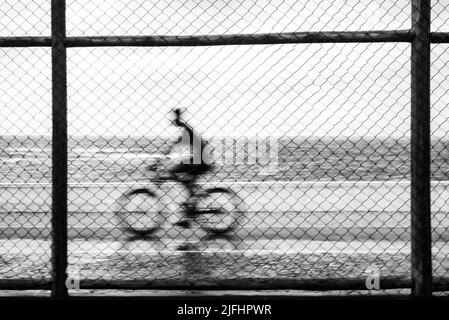 Silhouetten von Radfahrern, die bei Regen hinter dem Sportzaun vorbeifahren. Salvador, Bahia, Brasilien. Stockfoto