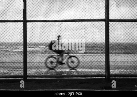 Silhouetten von Radfahrern, die bei Regen hinter dem Sportzaun vorbeifahren. Salvador, Bahia, Brasilien. Stockfoto