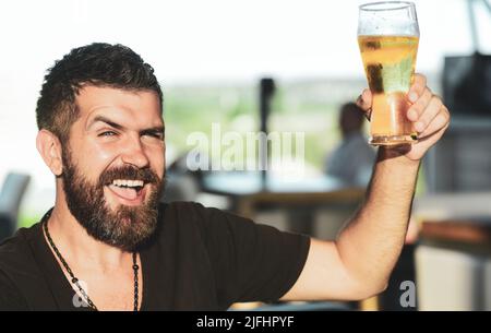 Ein hübscher Barkeeper hält ein Pint Bier in der Hand. Der Mann hält ein Glas Bier. Genießen Sie es im Pub. Bierzeit Stockfoto