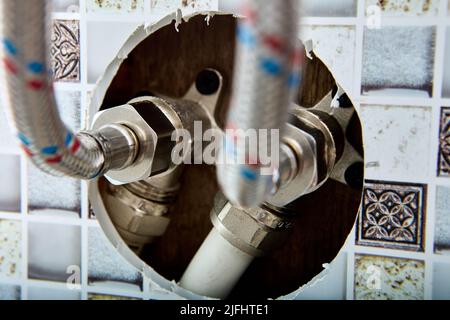 Sanitär-System, Anschluss von geflochtenen Schlauch Wasserleitung für die Lieferung von heißem und kaltem Wasser nach Hause kommt aus dem Loch in Wand des Hauses in der Landschaft. Stockfoto