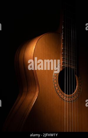 Spanische klassische Gitarre und Hände des Gitarristen aus nächster Nähe auf schwarzem Hintergrund mit Kopierraum und dramatischer Beleuchtung Stockfoto