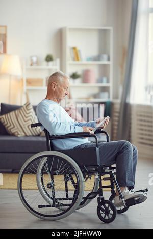 Seriös älterer Mann mit grauen Haaren sitzt im Rollstuhl und surft im Internet auf dem Tablet, während er Zeit zu Hause verbringt Stockfoto