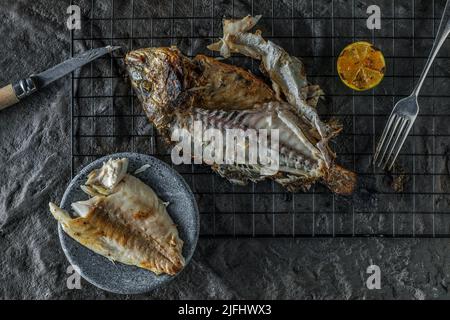 Ganze gegrillte Dorado mit gegrillter Limette oder Seebrasse auf dunklem strukturiertem Hintergrund. Gesunde Ernährung Konzept. Meeresfrüchte-Rezepte Stockfoto