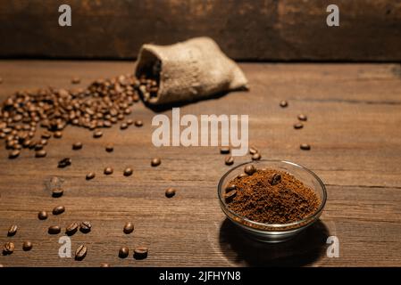 Selektive Fokussierung von frisch gerösteten Kaffeebohnen und gemahlenem Kaffee im Filterhalter auf Holztisch Stockfoto