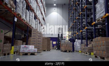 Moskau - Russland, 04.20.2022: Gabelstapler bewegt sich zwischen großen Metallregalen in einem modernen Lager und lädt Paletten mit Waren. Kreativ. Mitarbeiter Stockfoto