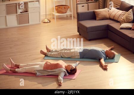 Müde ältere Paare liegen mit ausgestreckten Armen auf dem Boden, während sie sich in Shavasana entspannen Stockfoto