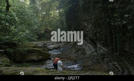 Blick in den dichten Wald und die Familie, die am bergigen Fluss mit Steinboden steht. Kreativ. Sommertourismus-Konzept. Stockfoto