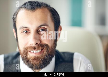 Porträt eines positiv stilvollen schönen jungen Mannes mit braunem Bart und Schnurrbart lächeln fröhlich im Büro Stockfoto