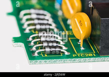 Halbleiterdioden und gelbe rückstellbare Sicherungen in Leiterplattendetails auf weißem Hintergrund. Nahaufnahme von elektronischen Komponenten auf grüner Leiterplatte. Stockfoto