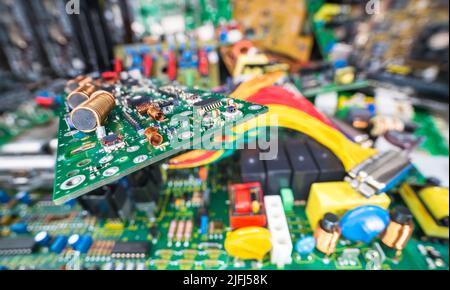 Leiterplatte auf verschwommenem E-Waste Stapel von ausrangierten Elektro- oder Computergeräten. Luft- oder Ferritkernspulen, Chips oder kleine Komponenten auf Kabel-TV-Verstärker-Leiterplatte. Stockfoto